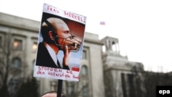 Ucraineni protestând în fața ambasadei ruse din Berlin cu o pancartă reprezentându-l pe Vladimir Putin cu botniță și textul --Doamna Merkel! opriți câinele nebun... 17 martie, 2014