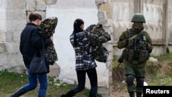 Femei din armata ucraineană, cu uniformele in brațe, trecând pe lângă un militar rus lângă Simferopol, astăzi 19 martie, 2014
